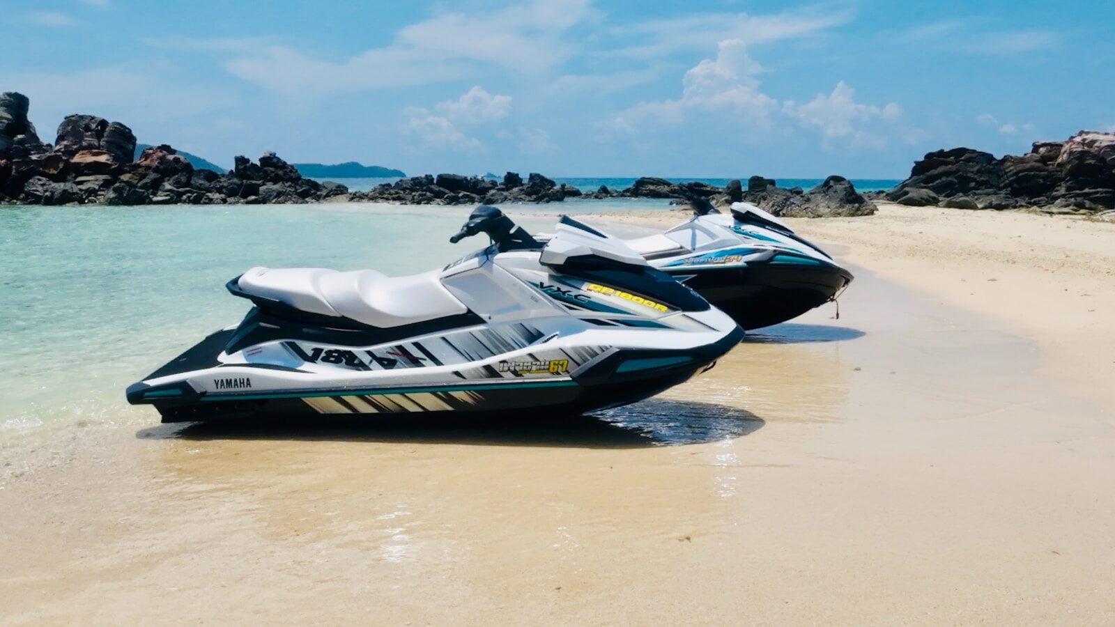 Two jet skis parked on a sandy beach.